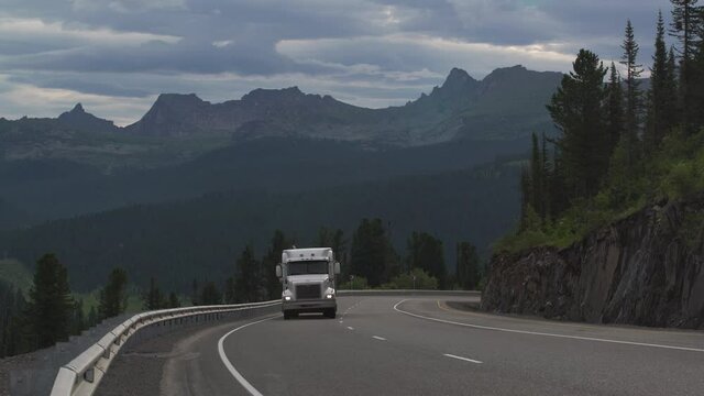 The road in the mountains. A large truck is climbing a mountain pass. A bend in a mountain road. Mountain pass. Nice turn in the road. Mountains in the background.  Siberia. Ergaki Natural Park.