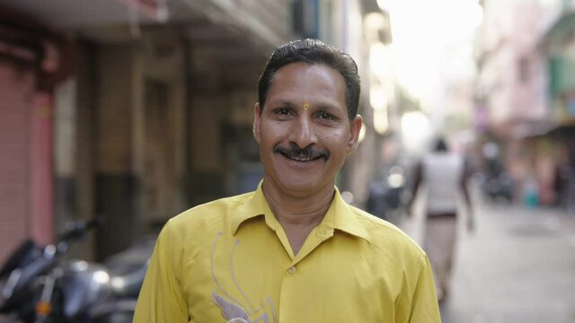 close view shot of a middle aged indian asian common man standing at the side of a urban local street and looking at camera 