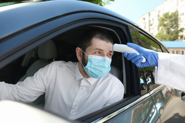 Doctor measuring driver's temperature with non contact infrared thermometer outdoors