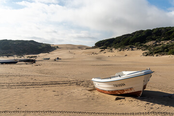 small wooden fishing rowboats on a sandy beach with a large sand dune in the background