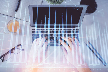 Double exposure of man's hands typing over laptop keyboard and forex chart hologram drawing. Top view. Financial markets concept.