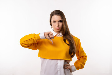 Portrait of attractive brunette girl showing thumb down. Human emotions, gesture concept. Studio shot, white background