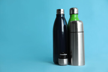 Stylish thermo bottles on light blue background, space for text