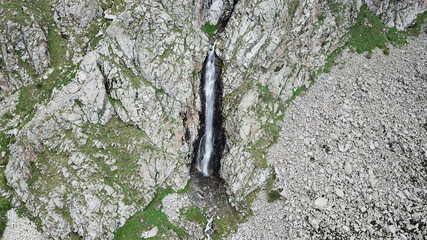 High waterfall among the rocks. View from a drone. Large rocks and steep slopes surround the...