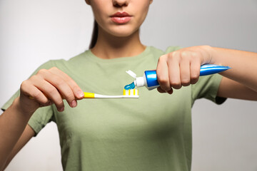 Woman applying toothpaste on brush against light background, closeup