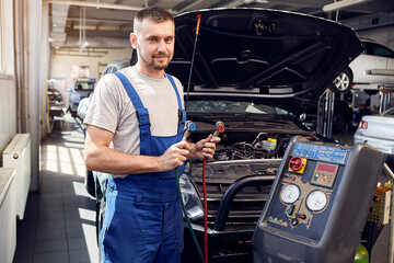 Mechanic holds a set of high-pressure pipes for filling the car's air conditioning system. A/C...