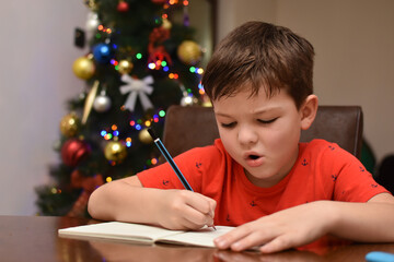 Beautiful young boy doing homework for holidays.
Kid studying on table in a living room