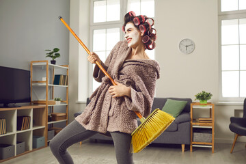 Cheerful young woman having fun with sweeping broom while cleaning her house. Funny crazy housewife...