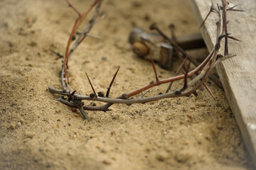 Crown of thorns, wooden plank and hammer with nails on sand. Easter attributes