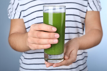 Woman holding glass with fresh celery juice on light blue background, closeup