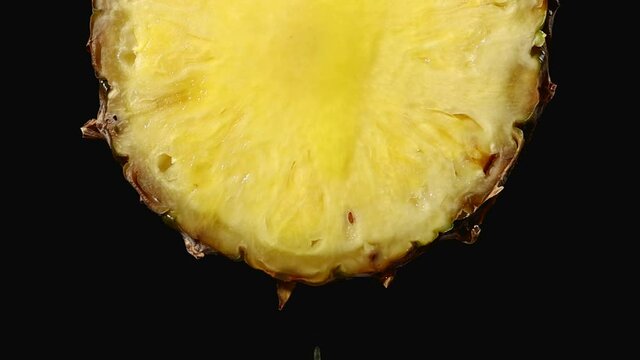 freshly squeezed pineapple juice flows from the ripe yellow fruit slice close - up on a black background slow motion