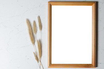 A wooden photo frame on a textured wall with stalks of fluffy dried grass.