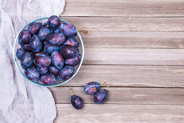 Top view of fresh organic ripe plums  in a glassy bowl and napkin  on wooden background with copy space. Flat lay.