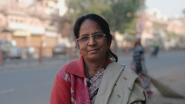 Close View Shot Of A Middle Aged Indian Asian Common Woman Wearing Specs And Traditional Saree With Smile On Face Standing At The Side Of A Urban Local Street And Looking At Camera 