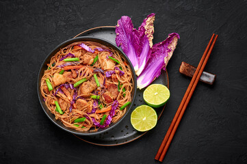 Pancit Bihon in black bowl on dark slate table top. Filipino cuisine noodles dish with pork belly, chicken, vegetables. Asian food. Top view