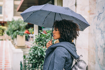 Attractive brunette with afro hair with an umbrella in front of a building