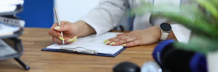 Female doctor holds pen in her hand and makes notes in medical documents. Health certificate