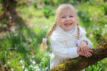 Cheerful little girl on a walk in the woods. Portrait of a girl among snowdrops. Bright sunny Easter day