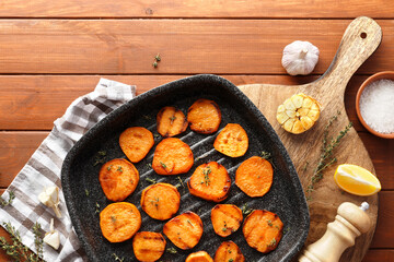 Delicious grilled sweet potatoes in a frying pan with ingredients on a wooden table