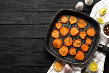Delicious grilled sweet potatoes in a frying pan with ingredients on a wooden table