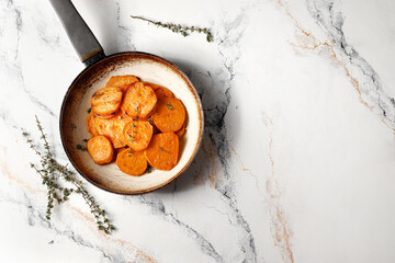 Frying pan with sweet potatoes, rosemary on a marble table