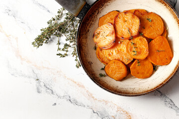 Frying pan with sweet potatoes, rosemary on a marble table