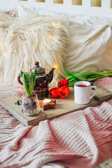 Obraz na płótnie Canvas Wooden tray with tea and spring flowers on a cozy bed, vertical photo. Breakfast concept