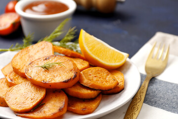 Plate with deliciously cooked sweet potatoes, rosemary, sauce on a textured background close up