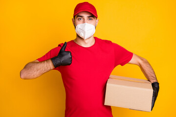 Fototapeta na wymiar Portrait of healthy guy wearing n95 respirator carrying parcel shop order showing thumbup isolated on vivid yellow color background