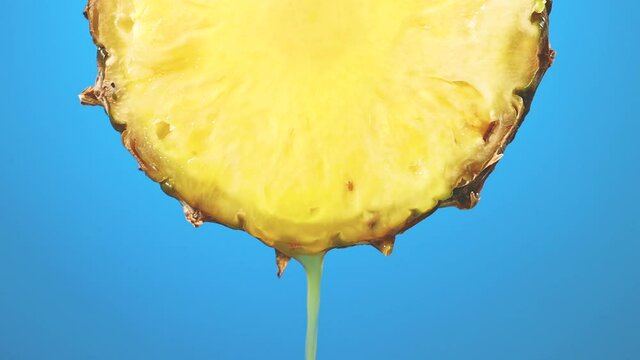freshly squeezed pineapple juice flows from the ripe yellow fruit slice close - up on a blue background slow motion