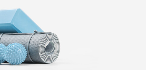 Rolled blue yoga mat and foam block or brick, massage ball. Gender neutral fitness and exercise concept accessories with copy space. Active lifestyle. Workout at home or gym, sports club banner