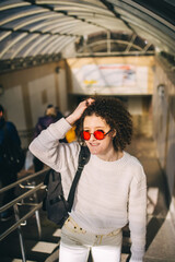 Young beautiful curly brunette woman in red glasses on escalator.