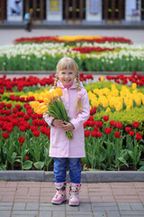 Funny little girl with a bouquet of fresh yellow tulips. A girl walks in the spring city
