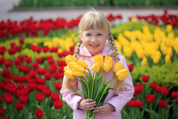 Portrait of a cheerful little girl on a background of tulips. Girl with a bouquet of yellow tulips. Spring sunny day