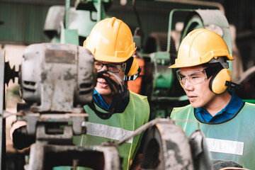 Work at factory.Two Asian workers man team working together in safety work wear with yellow helmet using Manual book.in factory workshop industry meeting professional