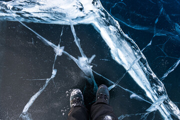 Traveler man in big tracking boots standing on surface of natural ice of Lake Baikal, Russia.