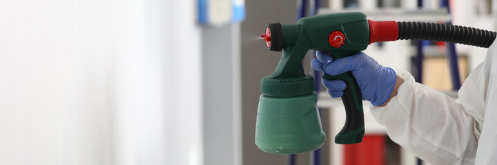 Man stands next to stepladder and holds spray gun in his hands. Wall painting concept