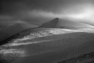 Grayscale. Snow covered mountain slope in last evening sunlight. Magnificent windy dusk on...
