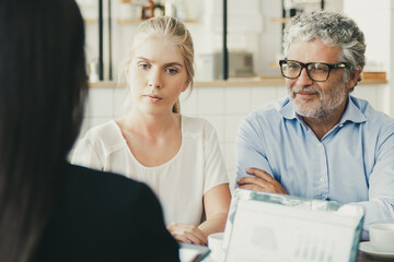 Obraz premium Young and mature customers meeting with financial expert. Back of businesswoman using laptop with graphs on display and talking to clients. Business meeting concept