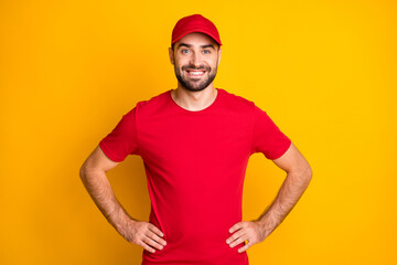Photo of cheerful confident delivery man wear red outfit smiling hands arms waist isolated yellow color background