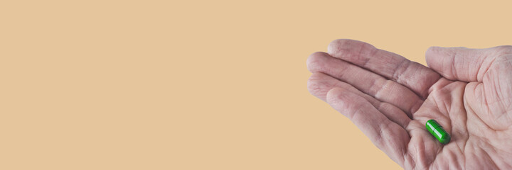 one green capsule with drug lie on a man's wrinkled palm, isolated image on background, banner concept