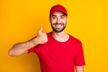 Fototapeta na wymiar Photo of handsome cheerful delivery man wear red outfit smiling showing thumb up isolated yellow color background
