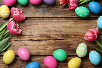 Obraz premium Frame of colorful eggs and tulips on wooden background, flat lay with space for text. Happy Easter