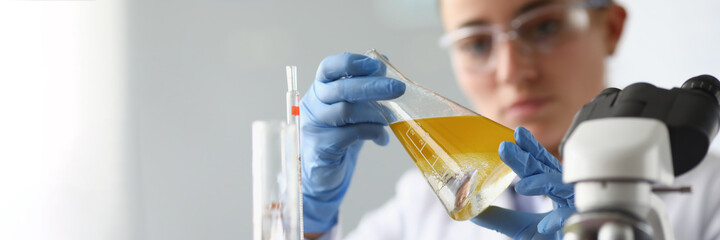 Woman chemist holds flask with yellow liquid in her hands in chemical laboratory. Quality control...