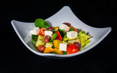 Fresh greek vegetable and cheese salad on white plate on black background