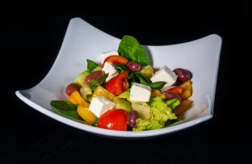 Fresh greek vegetable and cheese salad on white plate on black background