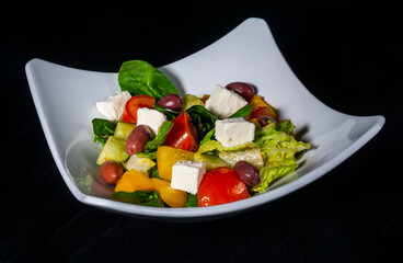 Fresh greek vegetable and cheese salad on white plate on black background
