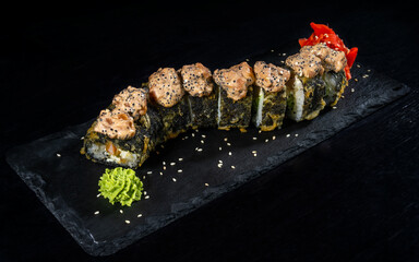 Dragon sushi set with ginger and wasabi sprinkled with grains on a black board and a solid background