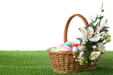 Fototapeta na wymiar Wicker basket with Easter eggs and beautiful flowers on green grass against white background. Space for text