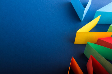 Multicolored cut paper on blue. Abstract arrows, direction signs.